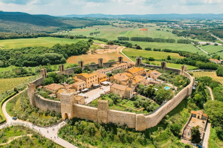 High aerial shot of the perfectly preserved medieval circular walls and stone towers of Monteriggioni surrounded by green countryside during a Baroque Bacchus tour in Tuscany