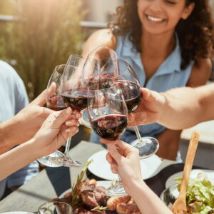 Group of happy people toasting with wine glasses filled with Tuscan red wine over a table with roast meat and salad during a Baroque Bacchus private tour