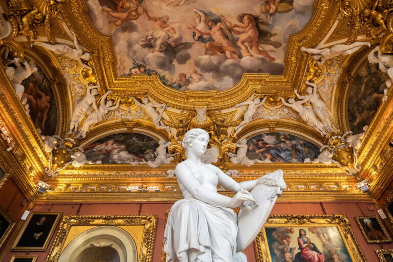 Classical white marble statue standing below an ornate gold-gilded ceiling with Renaissance frescoes at the Uffizi Gallery in Florence during a Baroque Bacchus private tour