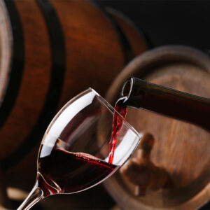 Close-up of rich red Tuscan wine pouring from a bottle into a clear glass inside a dimly lit cellar with traditional oak barrels during a Baroque Bacchus tasting tour