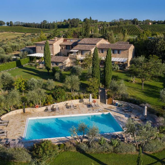 Sunny aerial view of a stone estate at Castello di Meleto with a large swimming pool, cypress trees, and rolling vineyards in Tuscany during a Baroque Bacchus tour