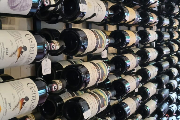 Horizontal display of premium Tuscan red wine bottles on a cellar rack including Castellare Chianti Classico during a Baroque Bacchus wine experience