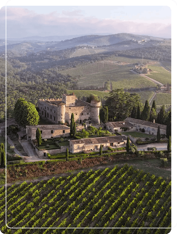 Breathtaking aerial view of the historic Castello di Meleto fortress surrounded by expansive vineyards and rolling Chianti hills during a Baroque Bacchus tour in Tuscany