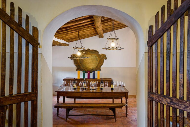 Atmospheric private wine tasting room with rustic wooden table, wine glasses, hanging chandeliers, and vaulted arch entrance in a Tuscan winery with Baroque Bacchus