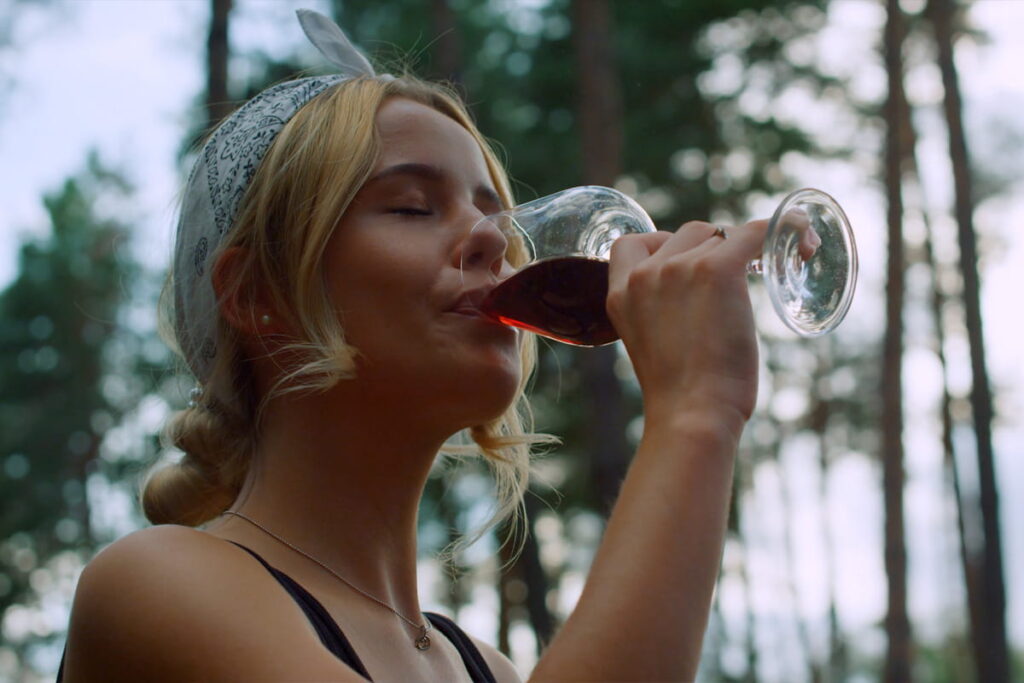 Young blonde woman enjoying a glass of red Tuscan wine with eyes closed amidst serene natural forest surroundings during a Baroque Bacchus private tour