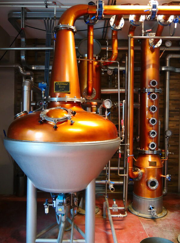 A shiny copper alembic still and distillation column used for traditional Italian grappa and spirits production during a private tour with Baroque Bacchus