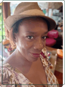 A close-up portrait of Melissa, wearing a stylish straw fedora and patterned dress, smiling warmly. A Baroque Bacchus founder.