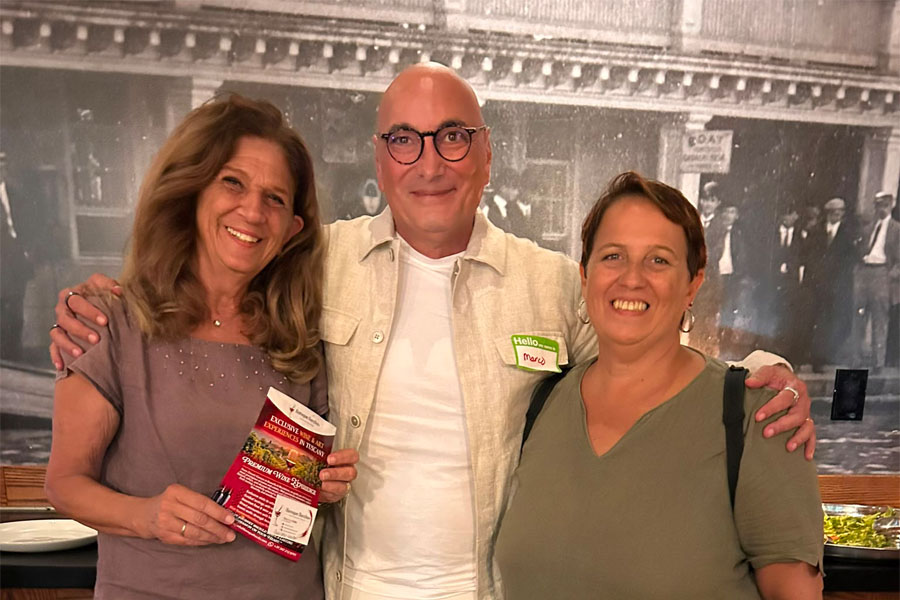 Baroque Bacchus co-founder Marco smiling alongside attendees while holding a Tuscan tour brochure at the West Orange Chamber of Commerce networking event