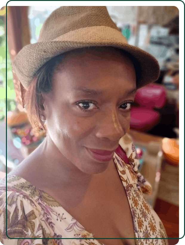A close-up portrait of Melissa, wearing a stylish straw fedora and patterned dress, smiling warmly. A Baroque Bacchus founder.